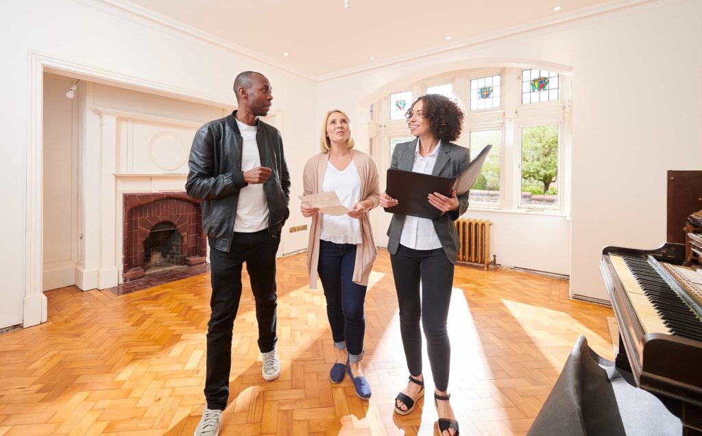 Real estate agent walks through a bright home with a couple during a property tour while discussing details and paperwork.