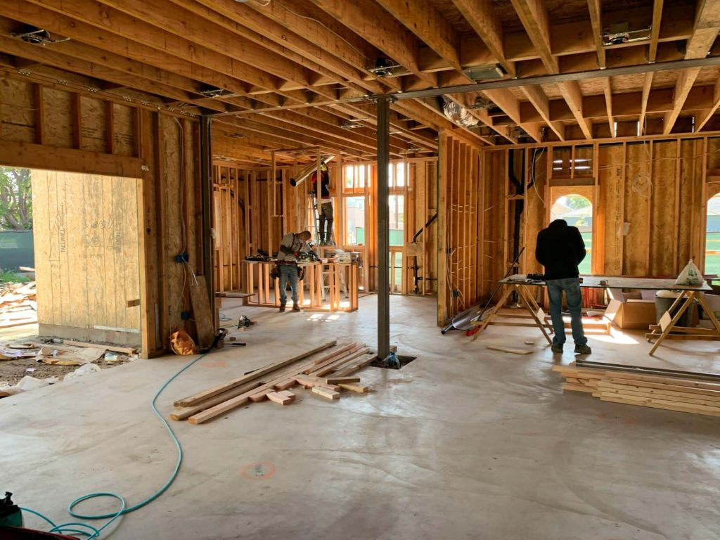 Interior of a home under construction with exposed wood framing, open floor plan, and workers building inside.