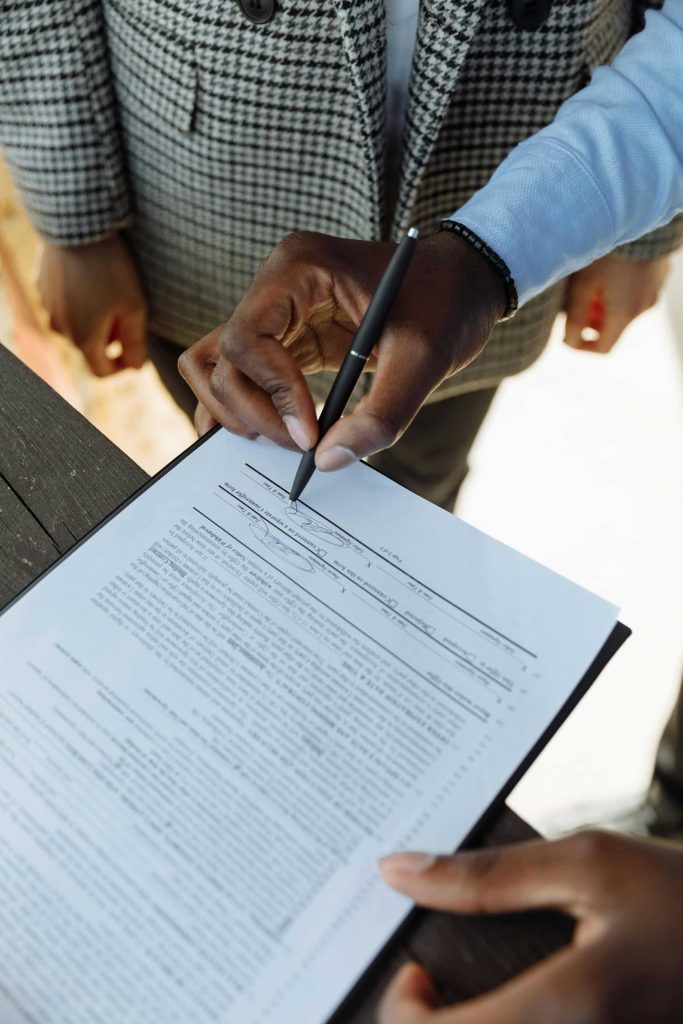 Close-up of people reviewing and signing paperwork on a clipboard with a pen.