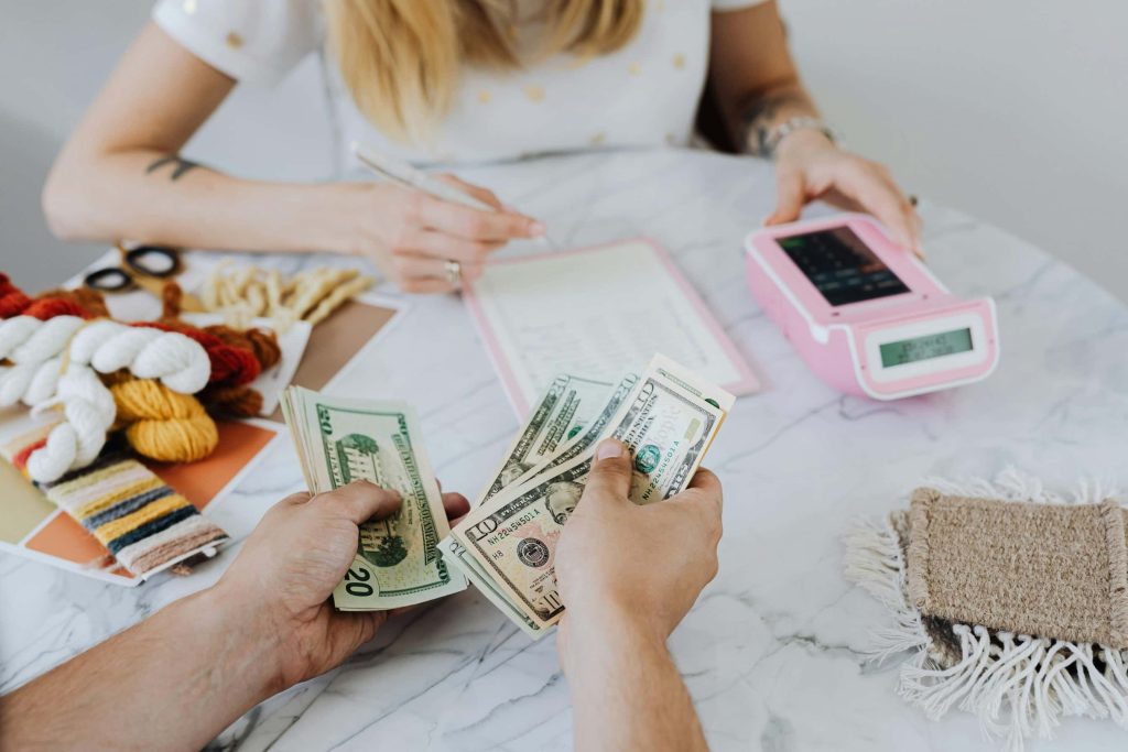 Person counts cash across a desk while another person writes on paperwork beside a card reader, representing refinancing or closing costs.
