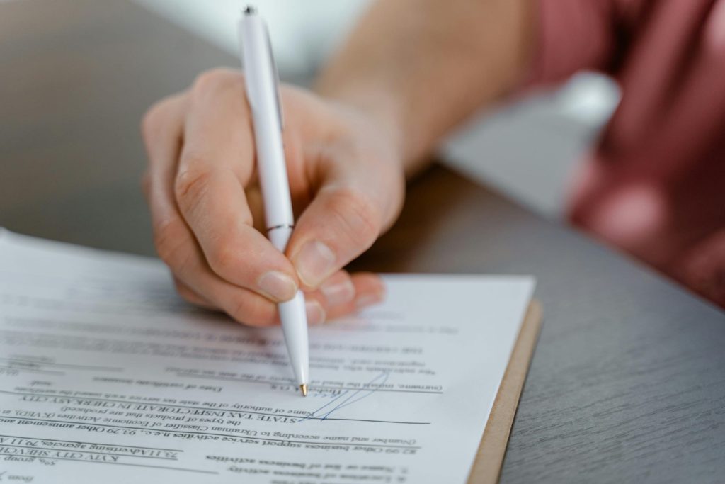 Close-up of a hand signing a legal document with a pen, representing title, escrow, or closing paperwork.