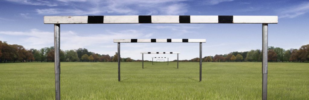 Series of hurdle-like barriers aligned across an open grassy field beneath a blue sky.