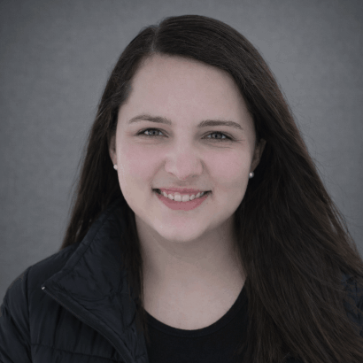 Professional headshot of a smiling woman with dark hair wearing a black jacket against a gray studio background.