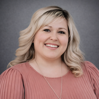 Professional headshot of a smiling blonde woman in a pink blouse against a gray studio background.