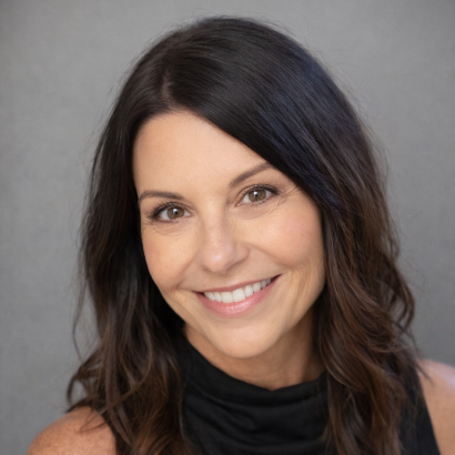Professional headshot of a smiling woman with dark brown hair wearing a black top against a gray studio background.