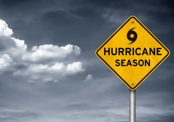 Yellow hurricane season warning sign against a cloudy sky, representing storm preparedness and property protection.