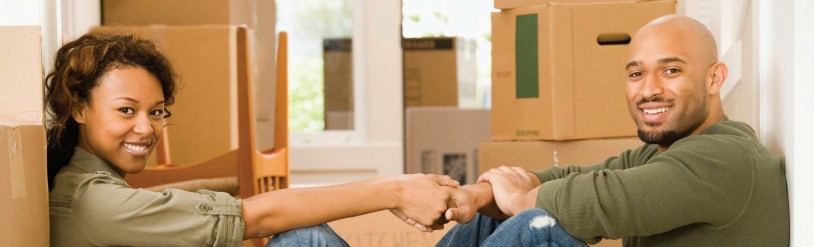 Smiling couple sitting among moving boxes and bumping fists in their new home during move-in.